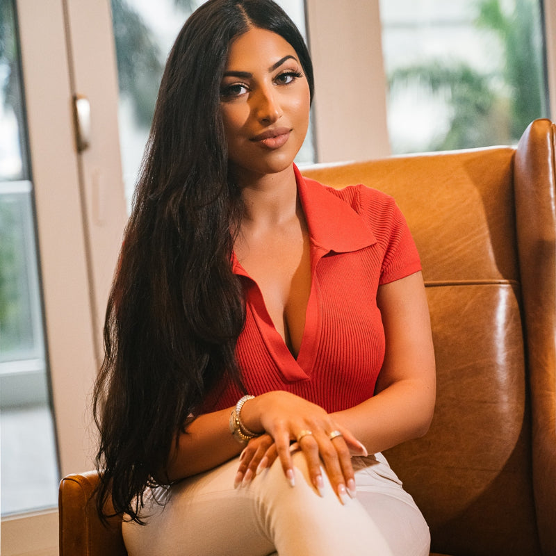 Professional woman in red ribbed top and white pants sitting in leather chair for lifestyle brand photography